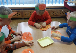 Dzieci przy stoliku wyklejają papierowe dynie bibułą